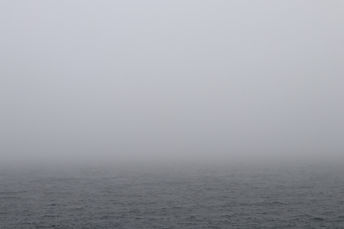 A thick layer of fog hangs over a grey ocean.