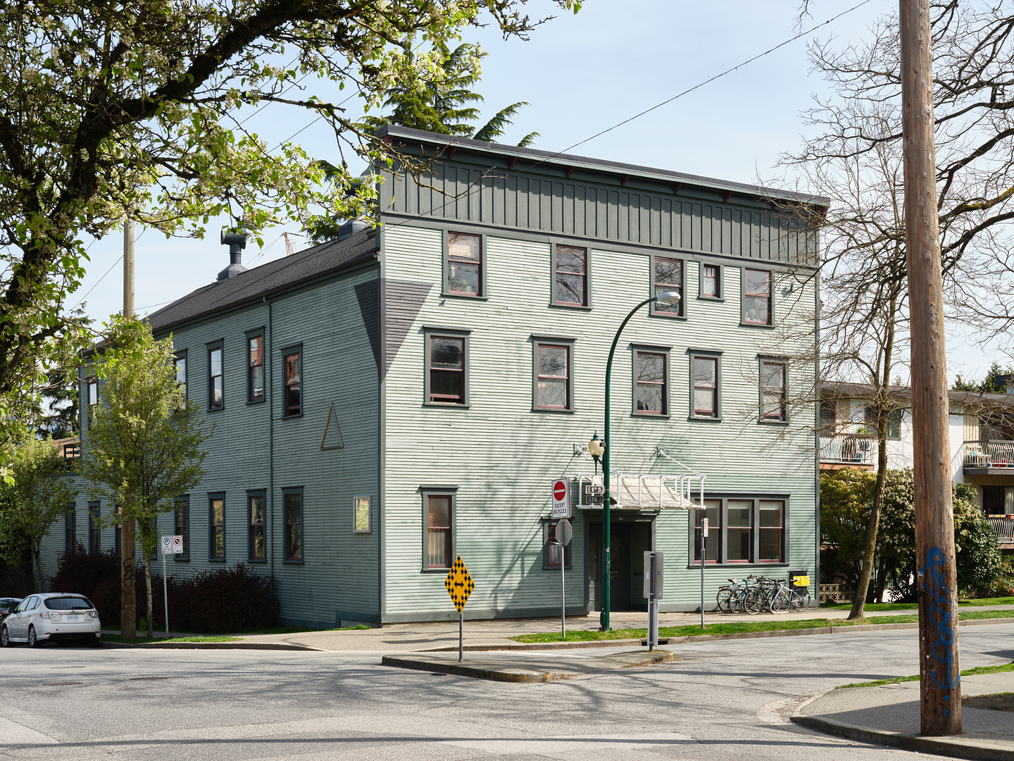 A colour photograph that looks north onto Western Front exterior, a large three story heritage building, with green wooden siding, and a false front façade. 
