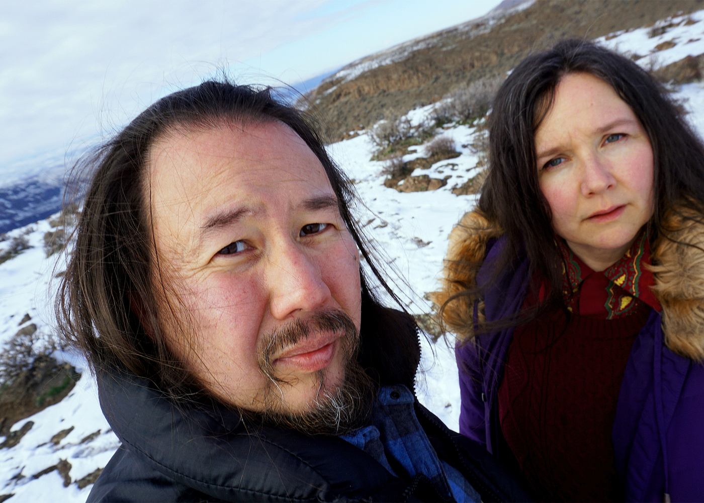 A selfie of Eyvind Kang and Jessika Kenney on a clear cold day. They wear winter jackets, and the ground around them is covered in snow.