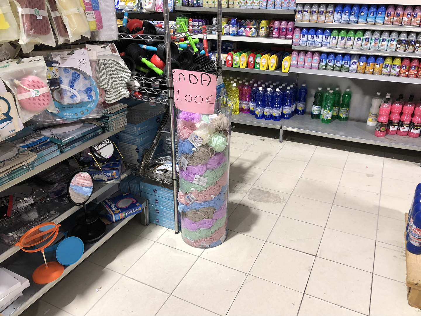 A cylindrical plastic tower of pastel loofahs stands in the aisle of a home goods store amongst various bath and body products.