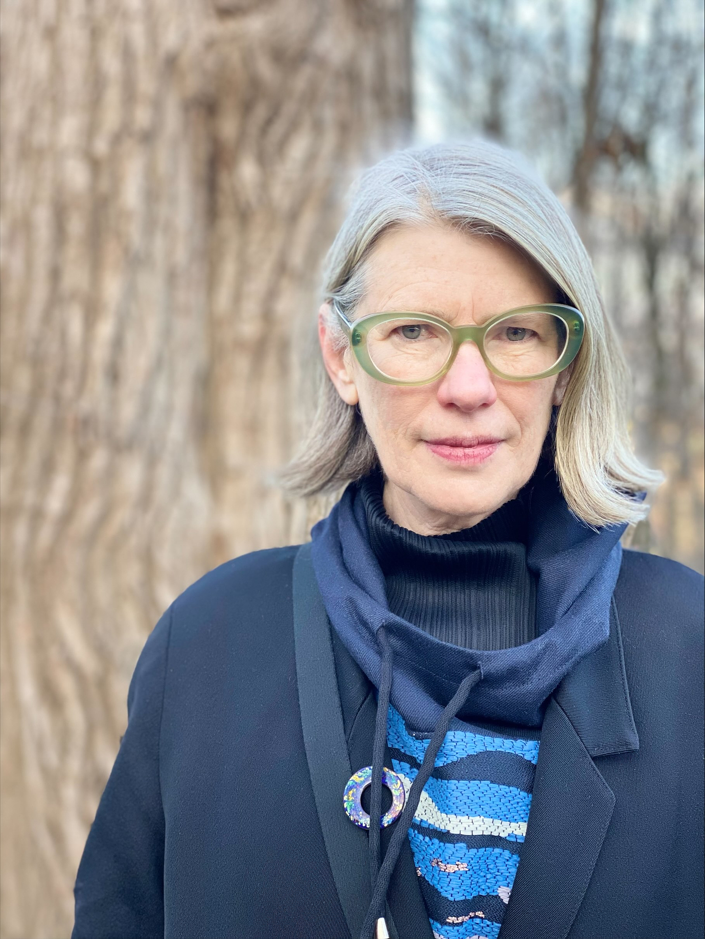 A portrait of Lisa Robertson. She is wearing green glasses and a blue blazer.