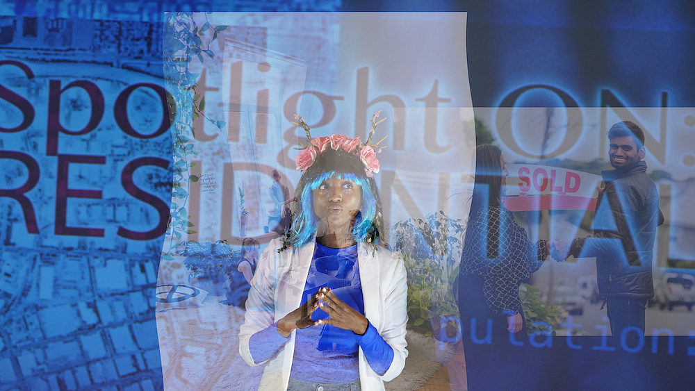 Lex Brown, wearing a blue shirt, white jacket, black and blue wig, and a crown of antlers and pink roses, stands in front of blue background of layered digital images including a satellite photograph of buildings near a river, a smiling man skating hands with a woman and holding a sign that says “sold” and the words “Spotlight ON: RESIDENTIAL” in large letters.