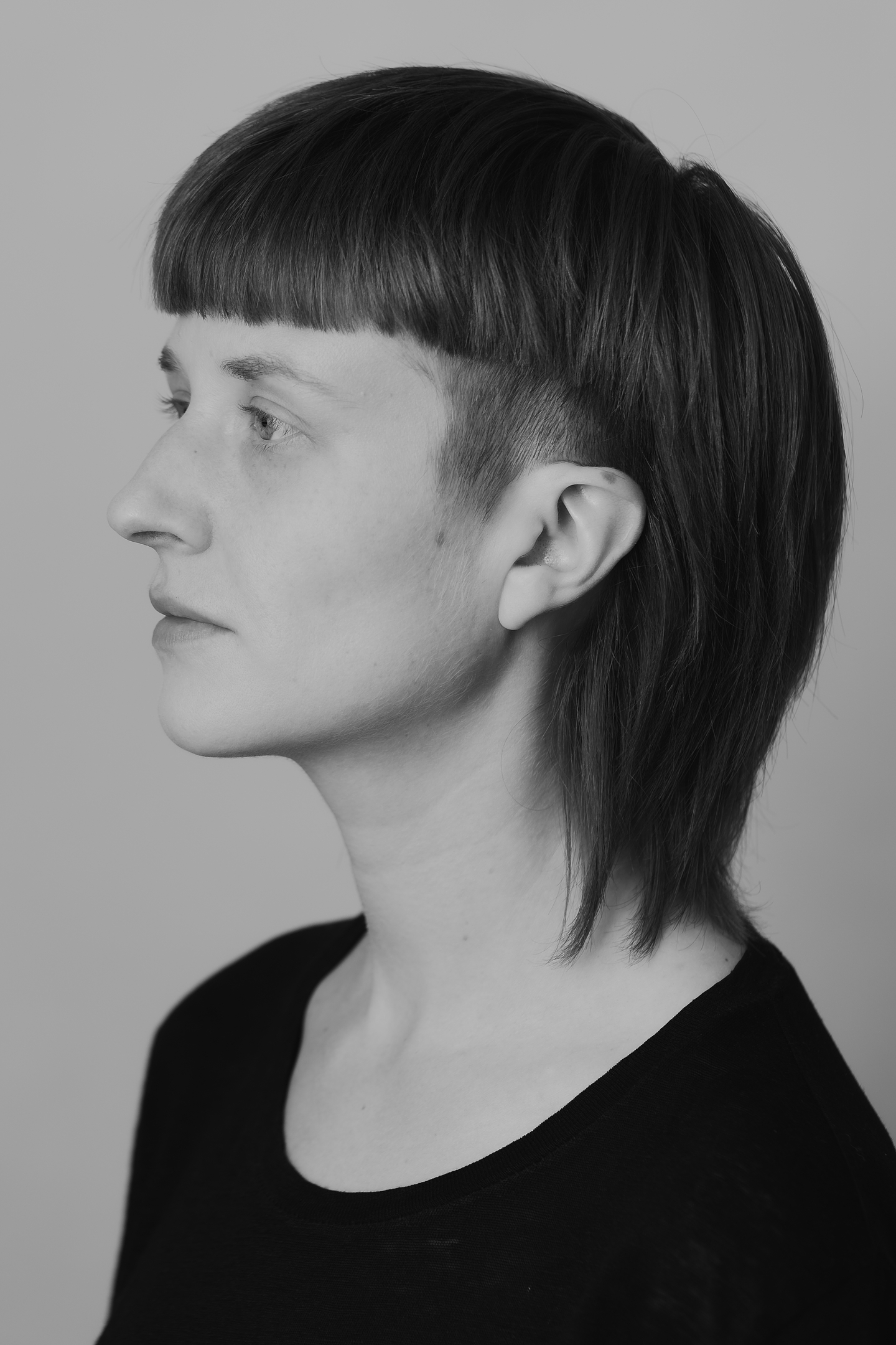 A black-and-white portrait of Klara Du Plessis in profile. She wears a black scoop-neck shirt and her hair is tucked behind her ear.