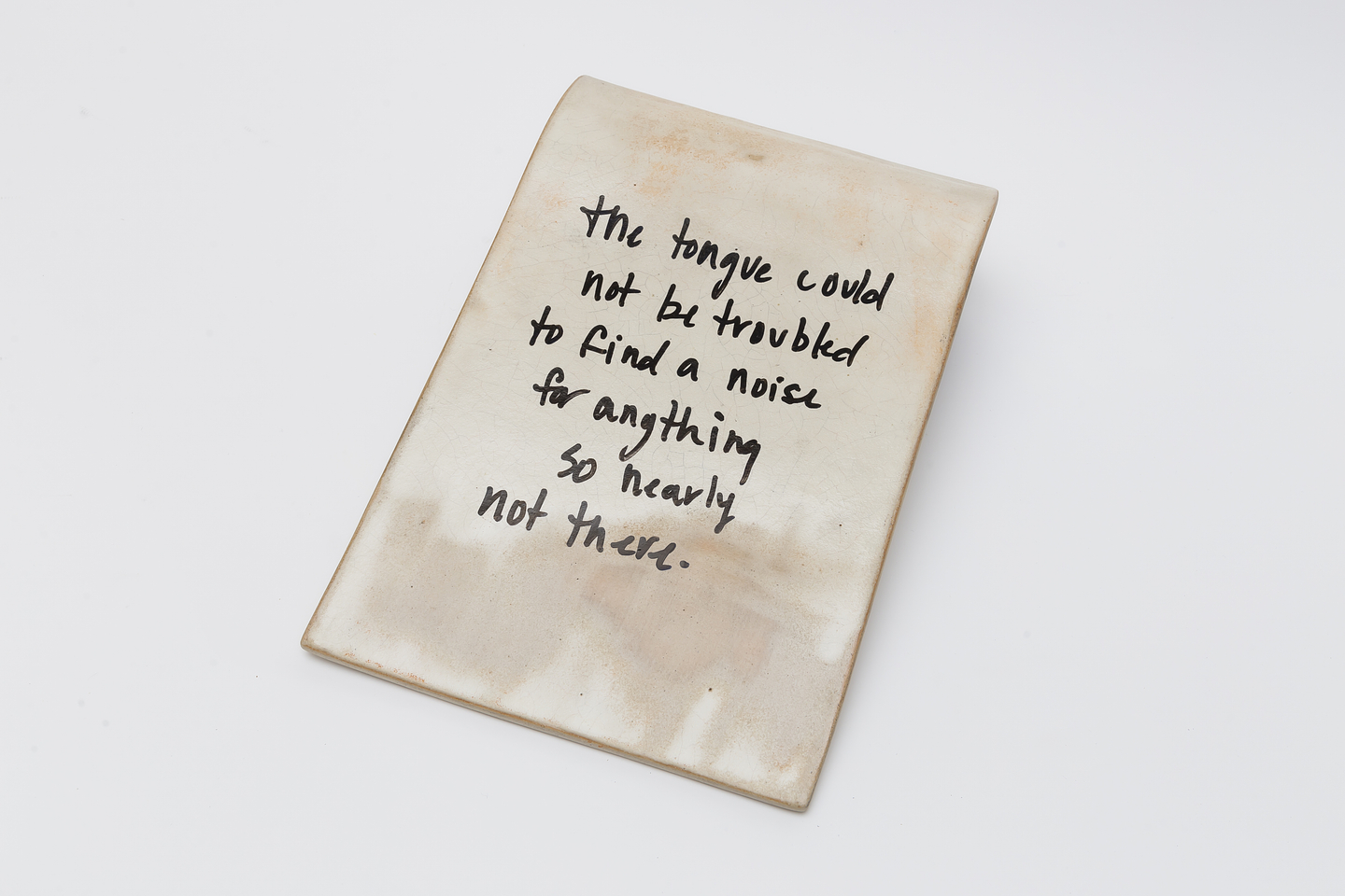 A ceramic slab by Rebecca La Marre with a soft curved shape and a light beige surface, featuring handwritten black text that reads: "the tongue could not be troubled to find a noise for anything so nearly not there." The text is slightly slanted and the slab has a subtly mottled, organic finish.