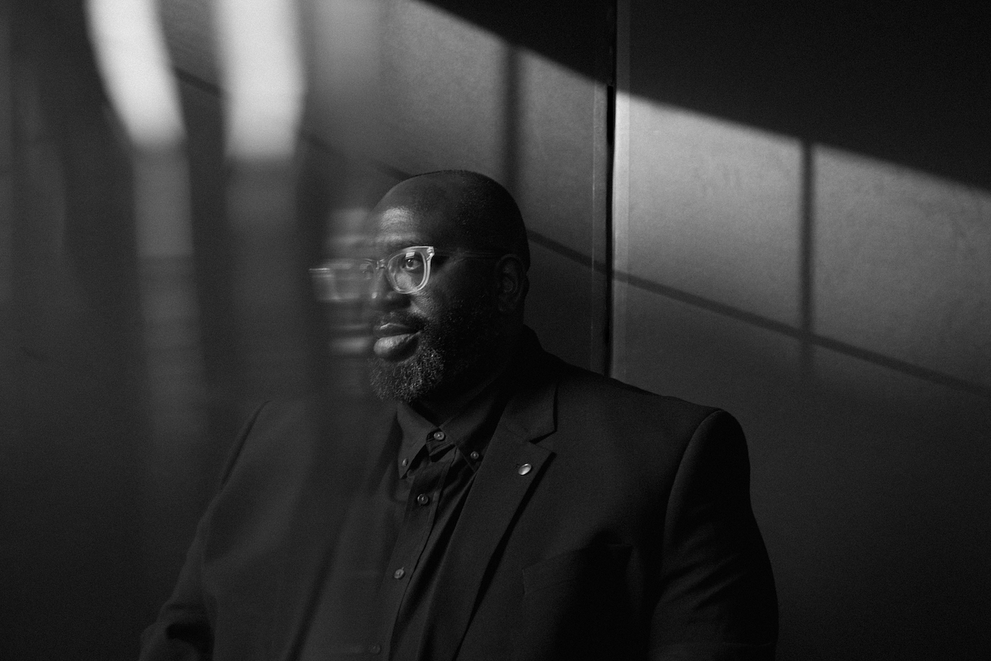 A portrait of Darius Jones in profile. A shaft of light falls onto his face, and cast a shadow of a window on the wall behind him.