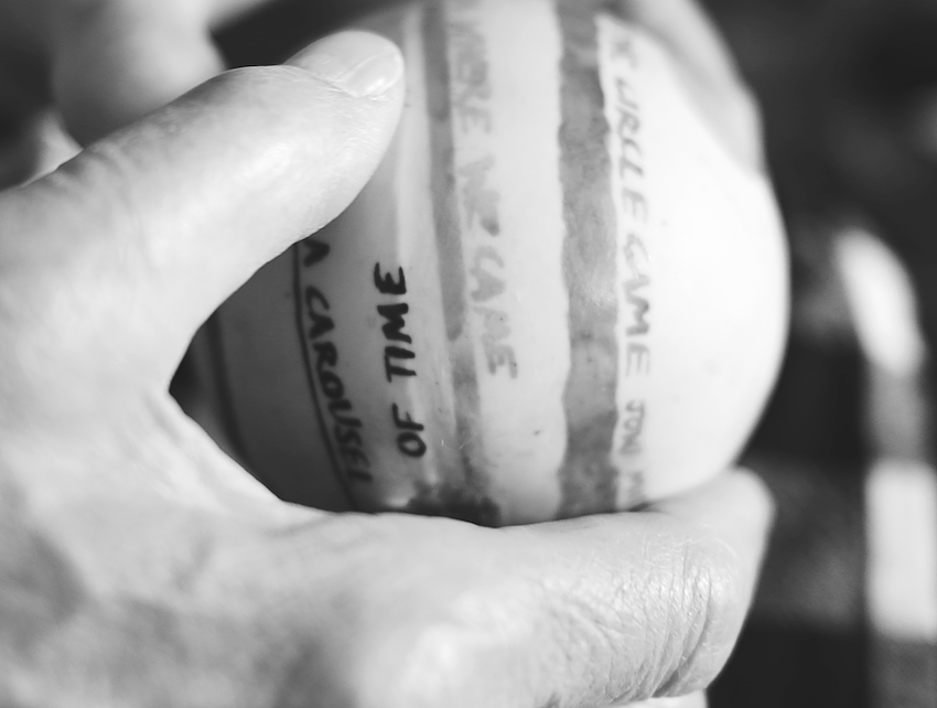 A black-and-white close-up photo of two hands gently holding a ceramic ball. The ball has several horizontal stripes, with handwritten text partially visible on the stripes. Some legible phrases include "ON A CAROUSEL" and "OF TIME." The image emphasizes texture and emotion through the focus on the hands and the worn writing on the ball.