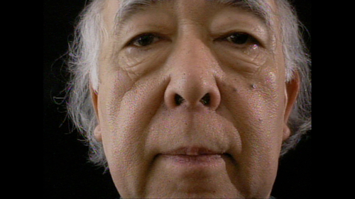 Close-up of the artist Nobuo Kubota who is looking directly into the camera, face filling the frame against a dark background.
