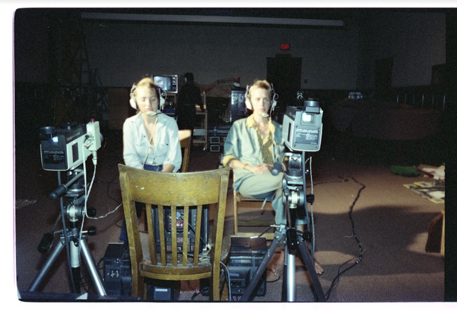 A colour photograph of two women, each seated, wearing headphones, and facing a video camera mounted on a tripod.