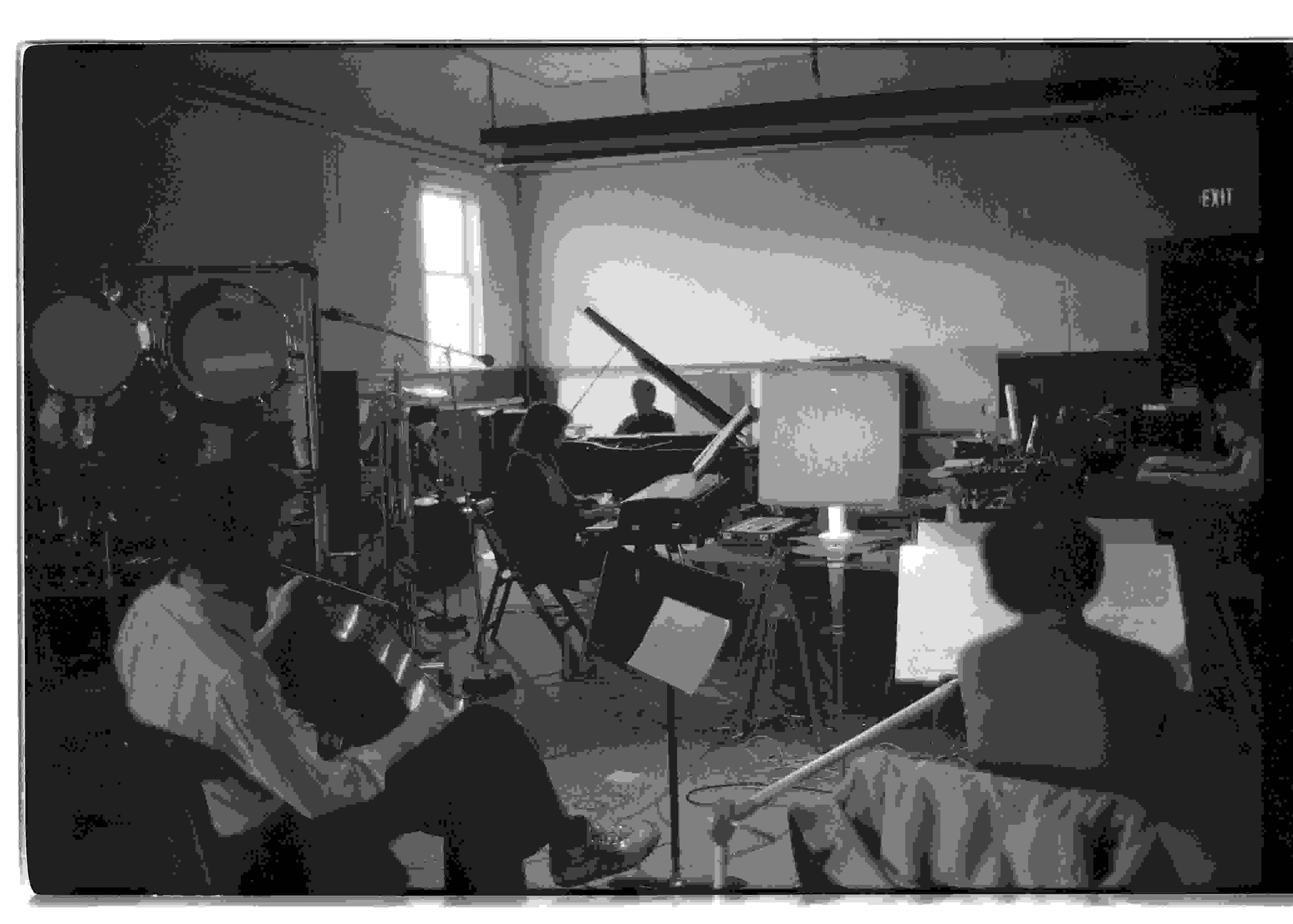 A black and white photo of musicians seated with their instruments in Western Front’s Grand Luxe Hall, including a pianist, keyboardist, cellist and vocalist.